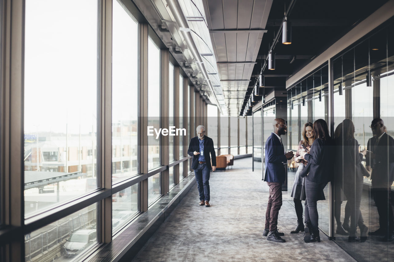 Smiling entrepreneurs talking while colleague walking in office corridor