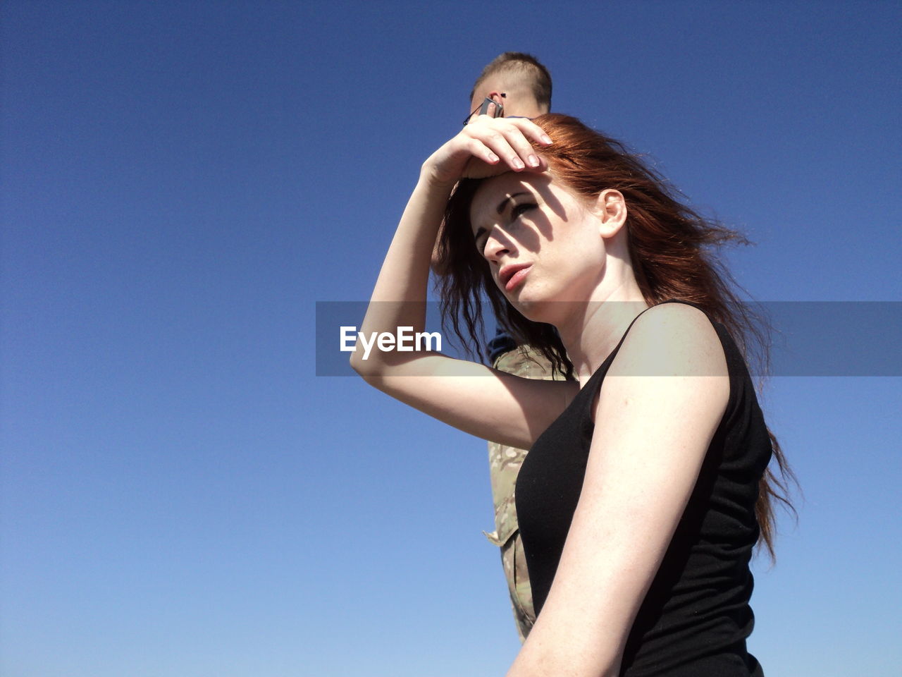 Young woman shielding eyes against clear blue sky