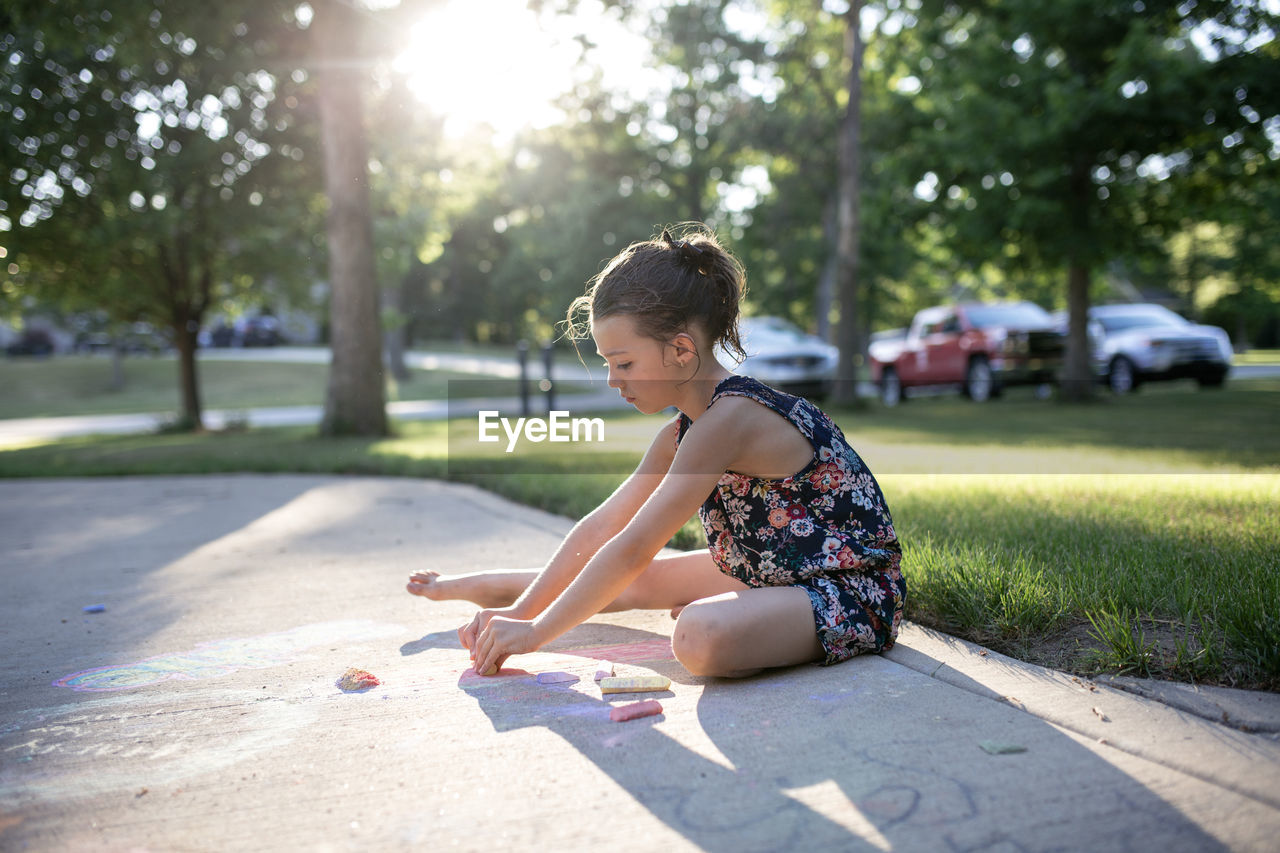 Side view of girl drawing with chalks on footpath at yard