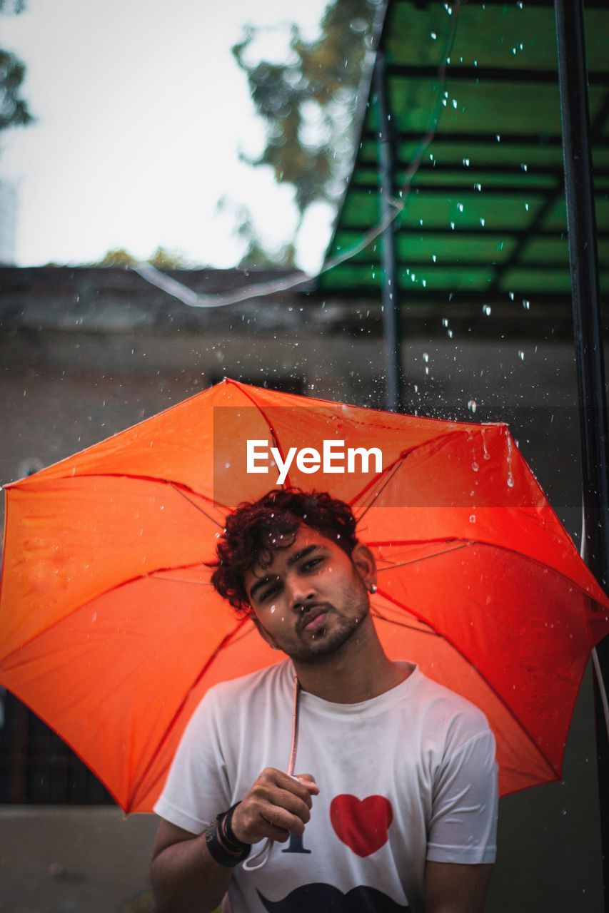 MAN HOLDING UMBRELLA STANDING ON WET RAINY DAY DURING MONSOON