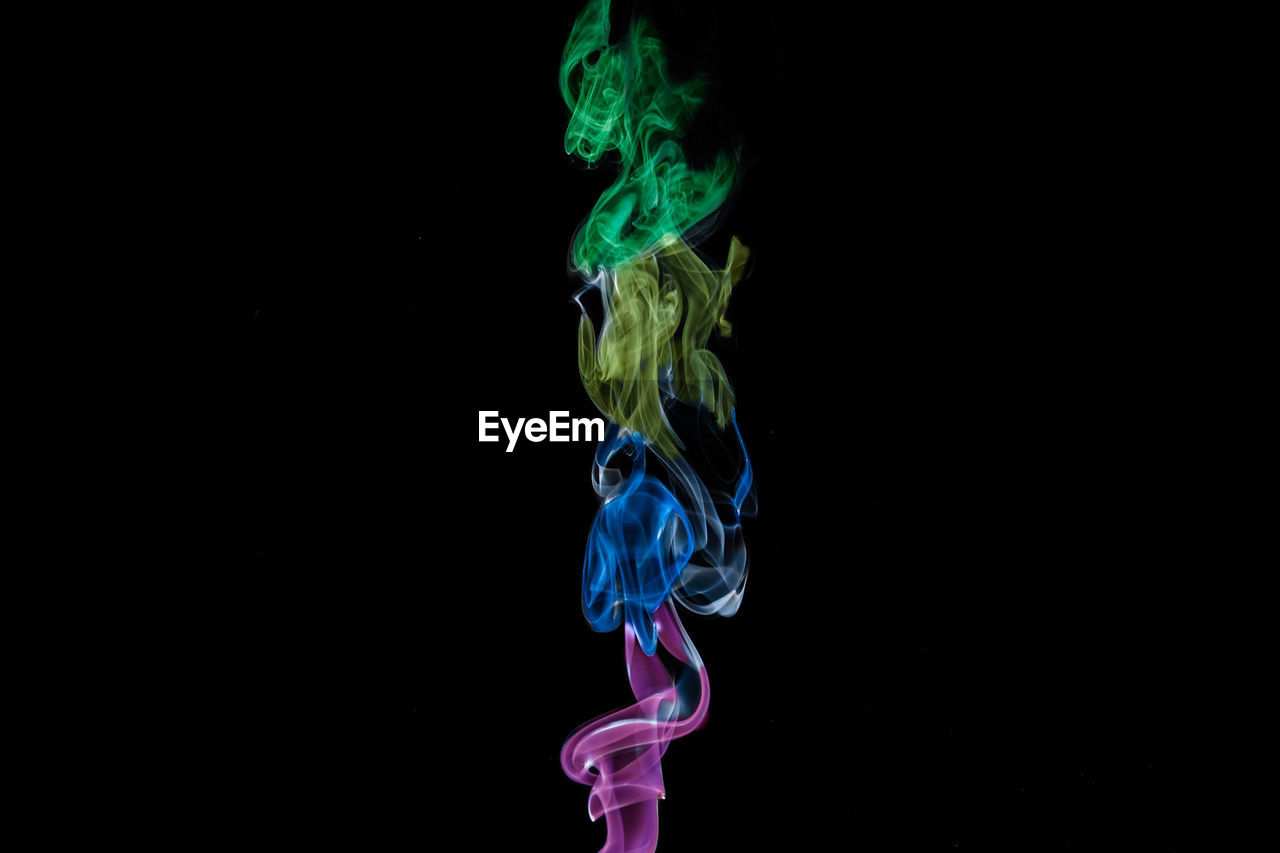 Close-up of multi colored illuminated smoke against black background