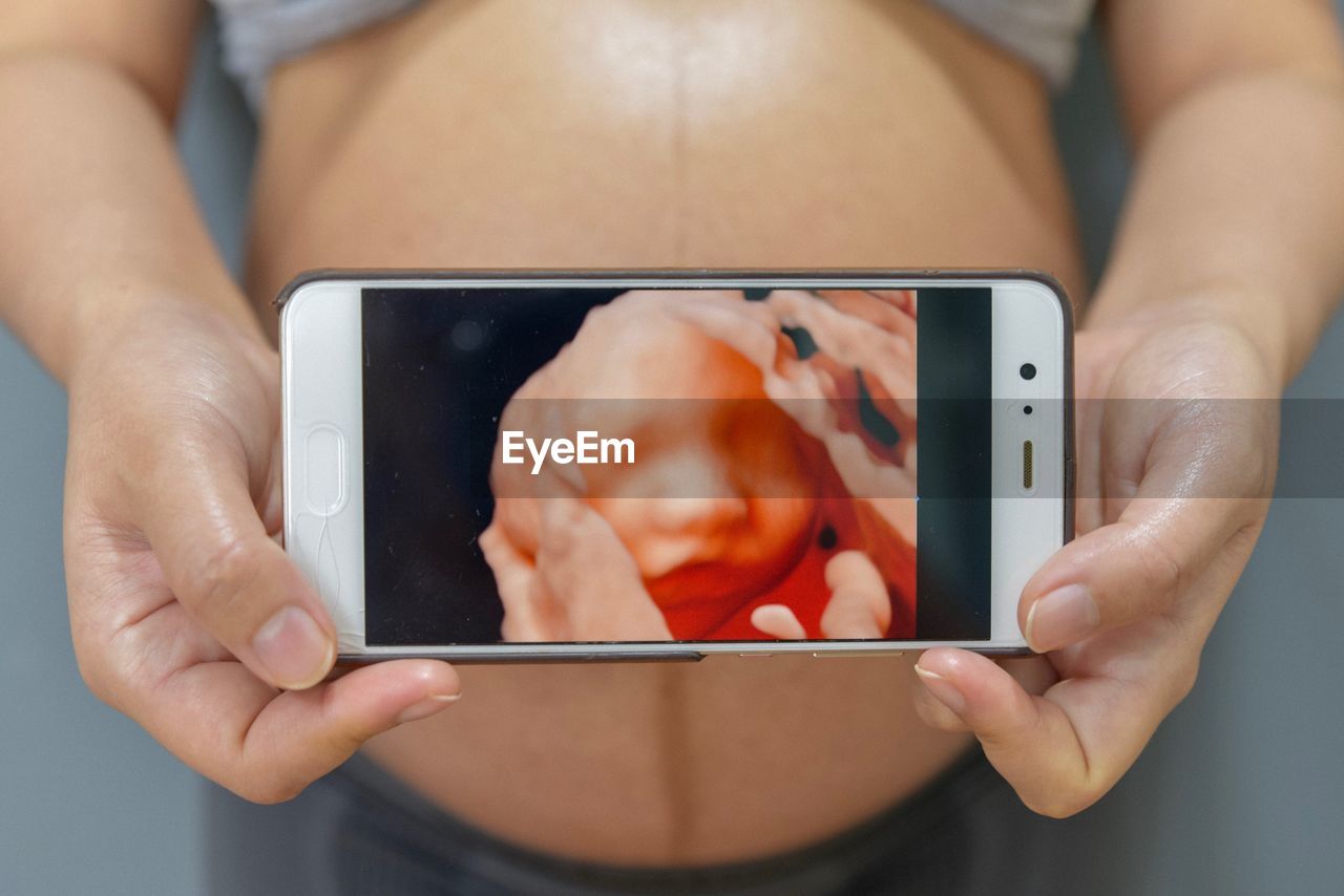 Midsection of pregnant woman holding mobile phone with baby ultrasound