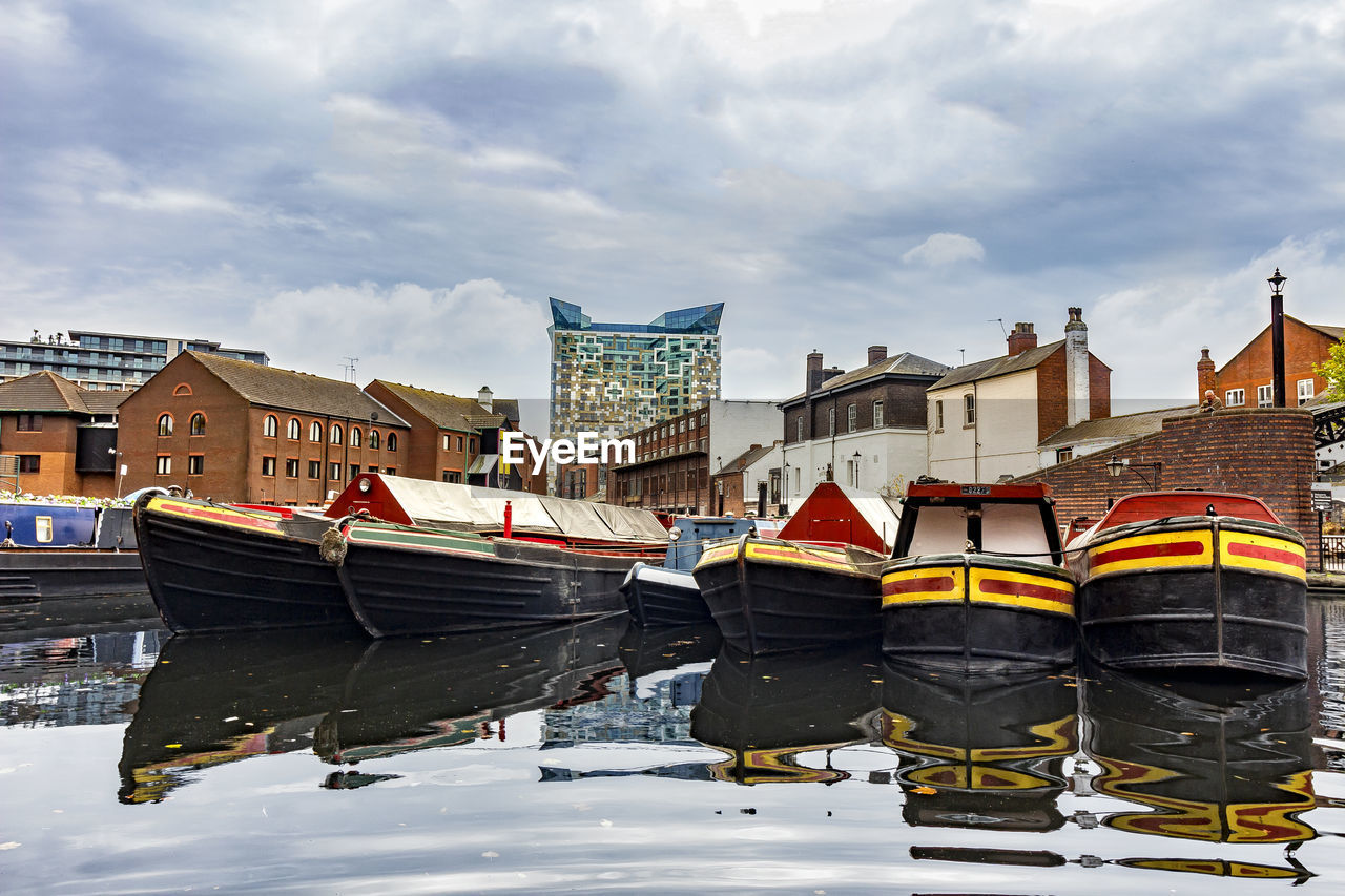 BOATS MOORED IN RIVER BY BUILDINGS AGAINST SKY