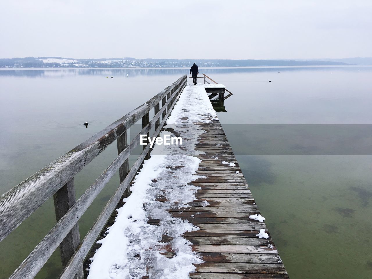 Woman walking on pier at sea against sky during winter