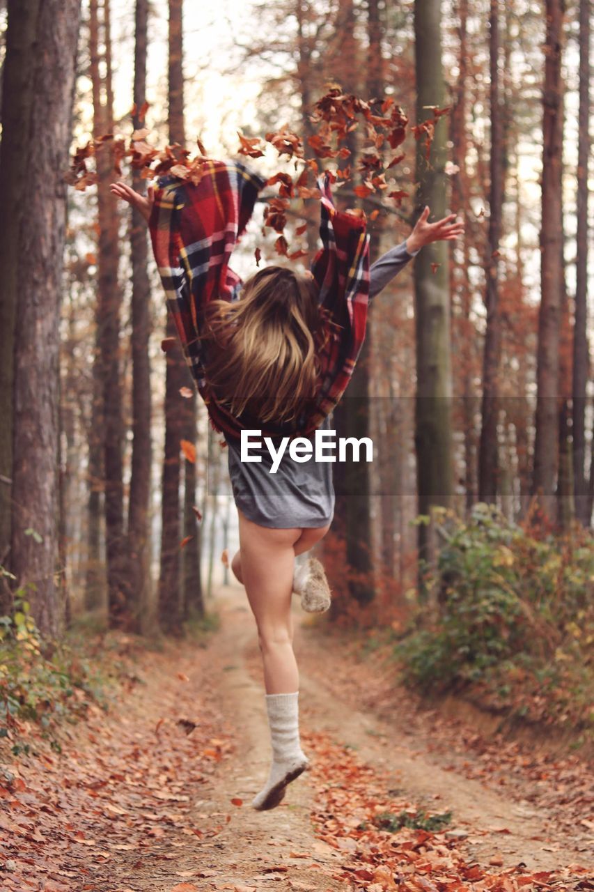 Young woman jumping and throwing leaves in the air in the forest 