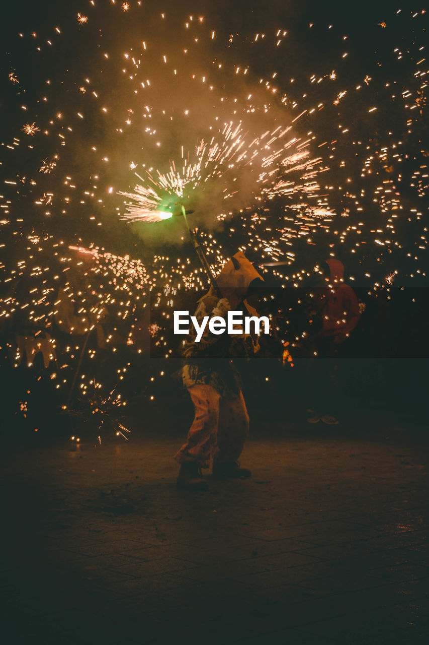 Man holding sparkler while standing outdoors at night