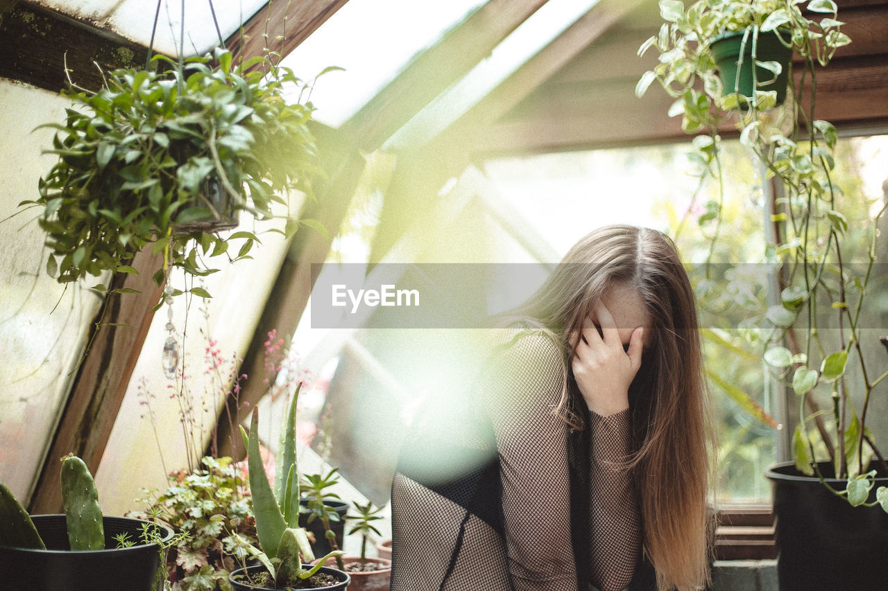 Young woman standing against plants covering her face