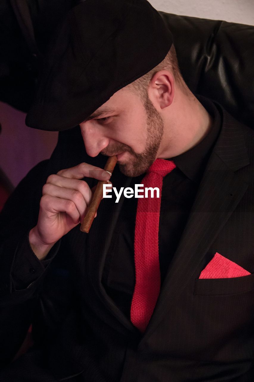 Close-up of man smoking cigar while sitting on sofa at home