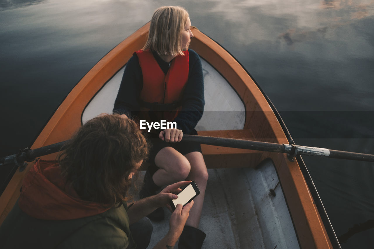 Woman rowing boat while man using mobile phone on lake