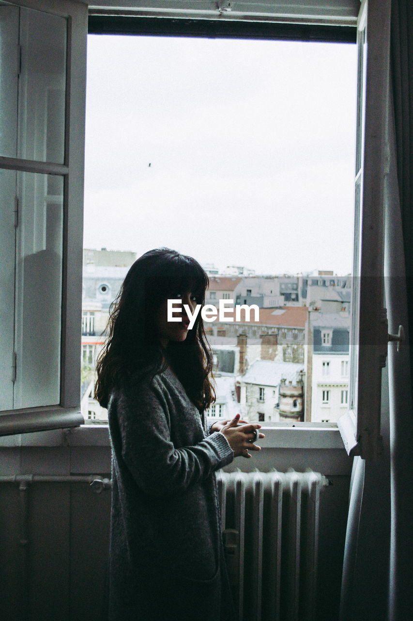 Young woman standing by window at home