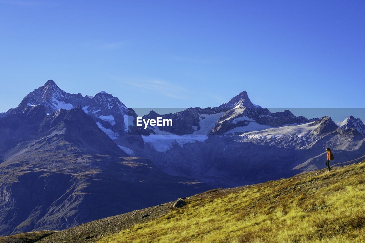 Woman walking on field by snow covered mountains against sky