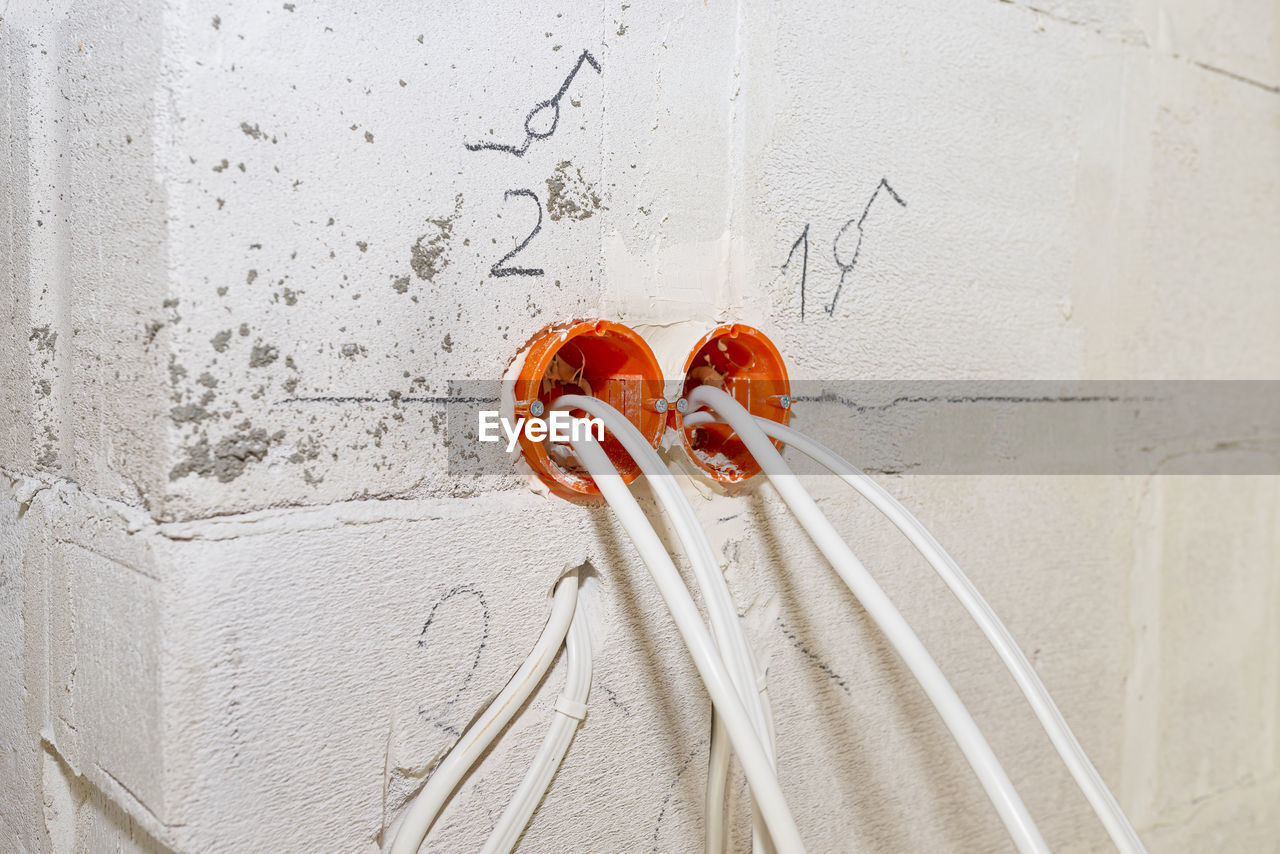 Orange, round junction box mounted in the white wall with protruding electric cables.