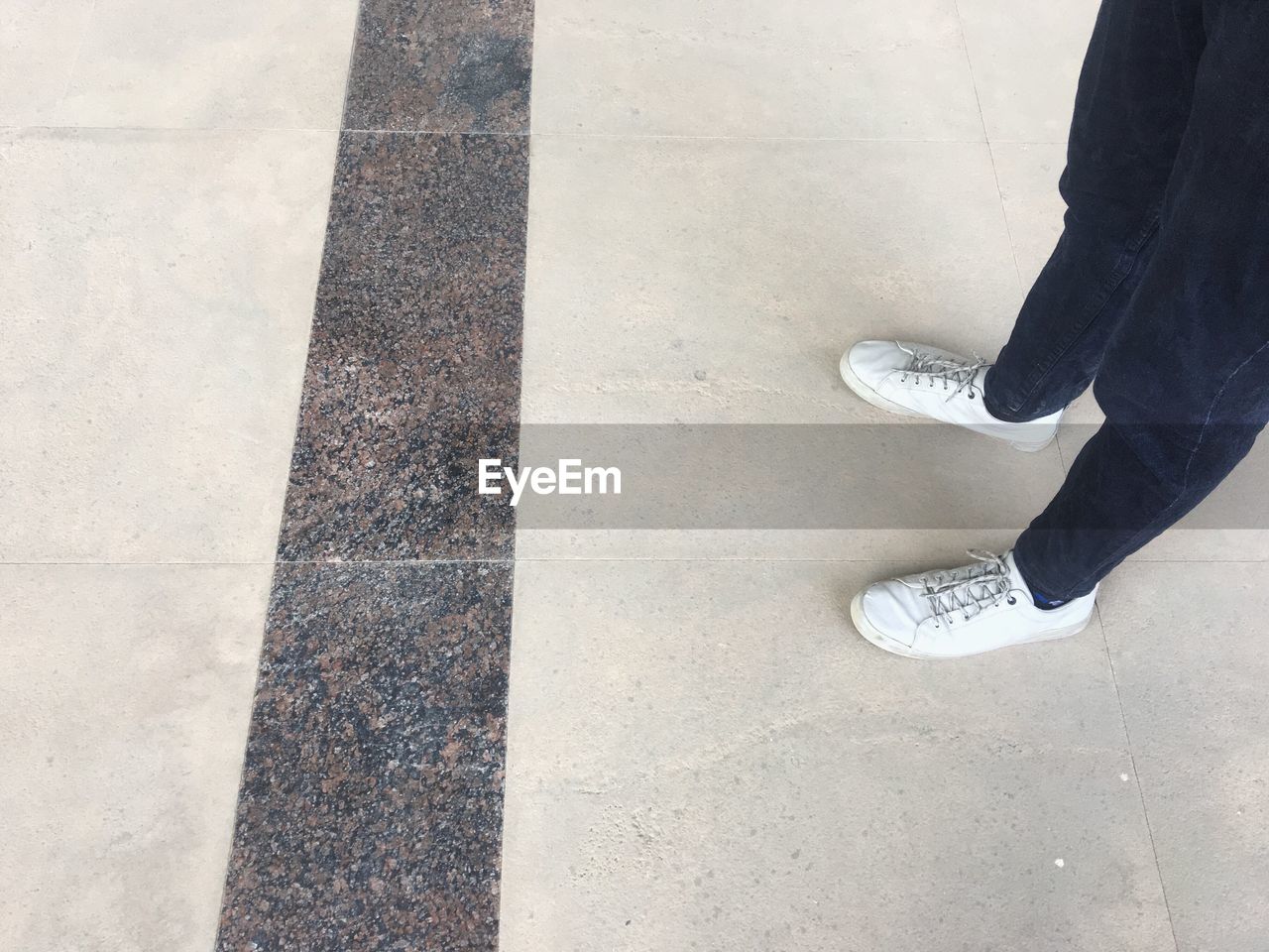 LOW SECTION OF MAN WALKING ON TILED FLOOR