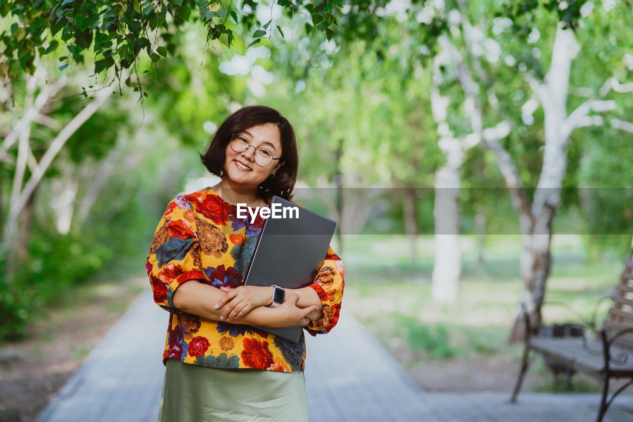 Confident young professional woman with laptop in summer city park