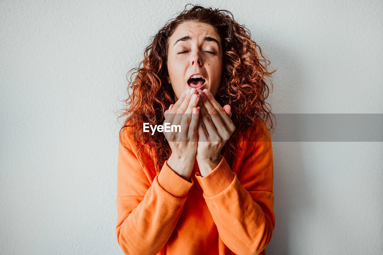 Woman sneezing while standing against wall