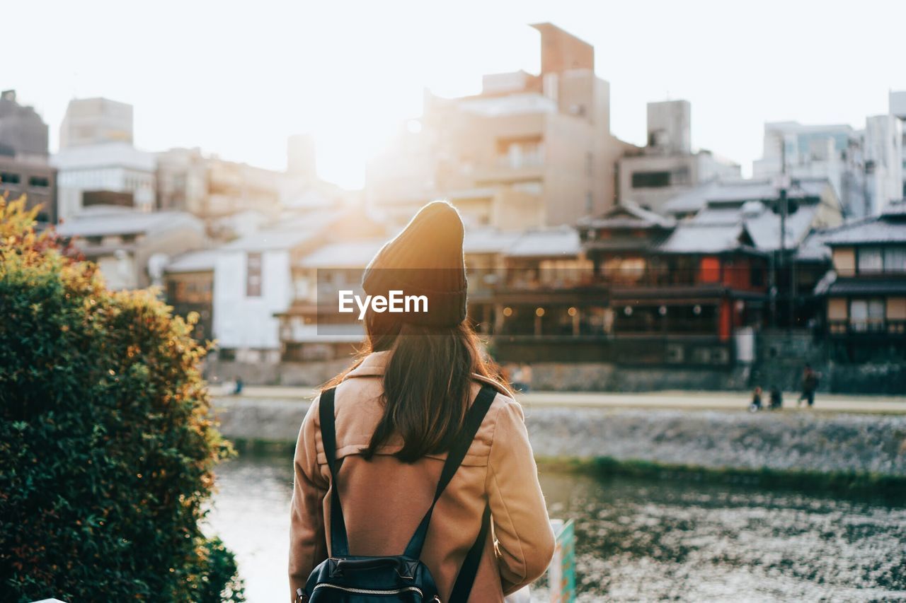 Rear view of woman standing by river and buildings in city