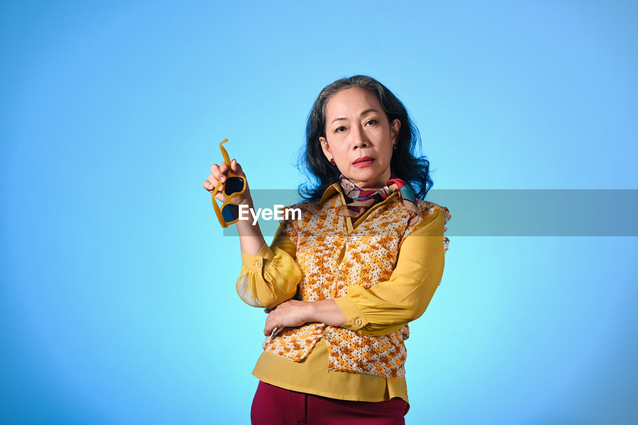portrait of young woman with arms raised against blue background