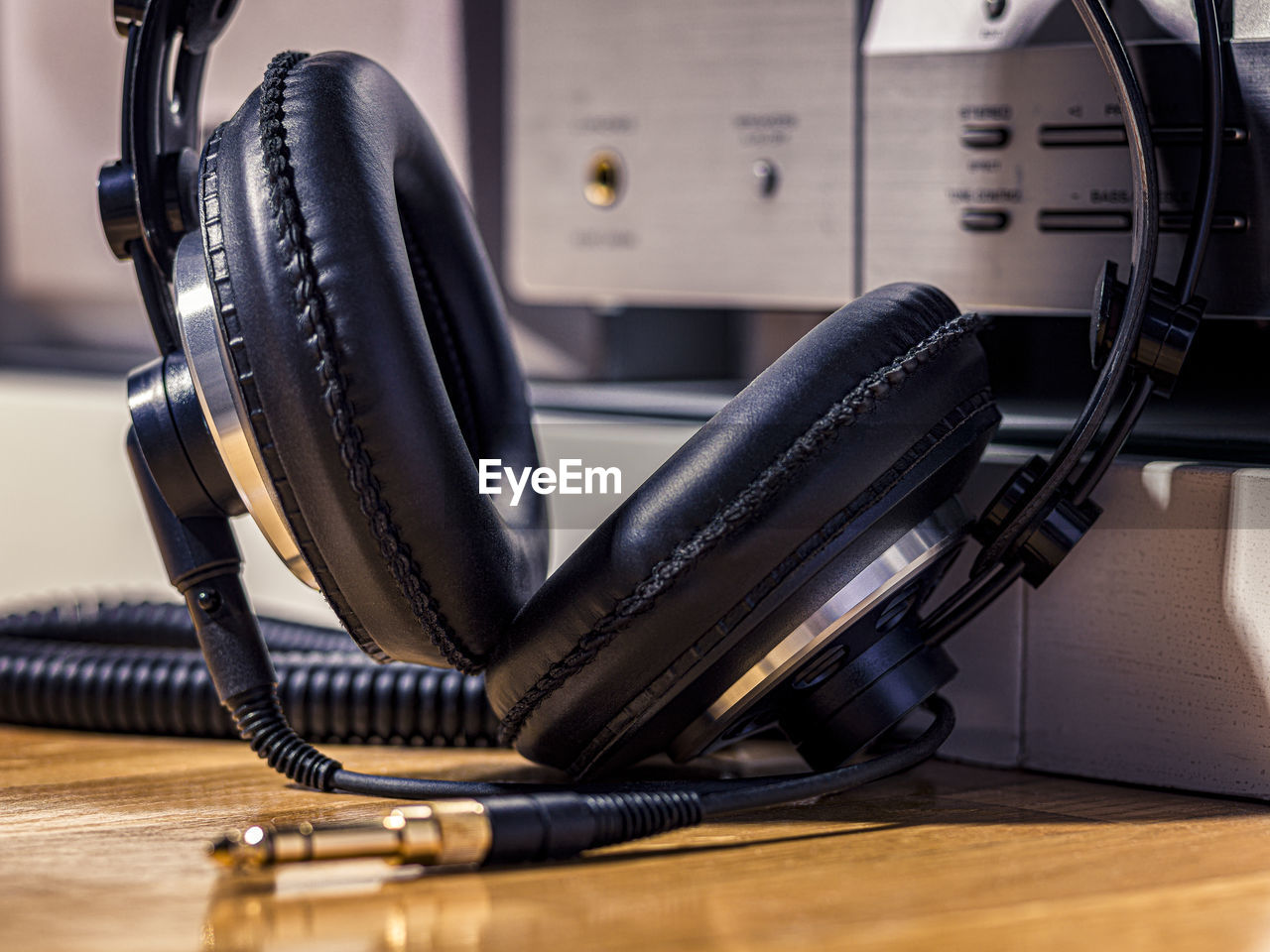 Black hi-fi headphones with a gold input jack on a wooden floor