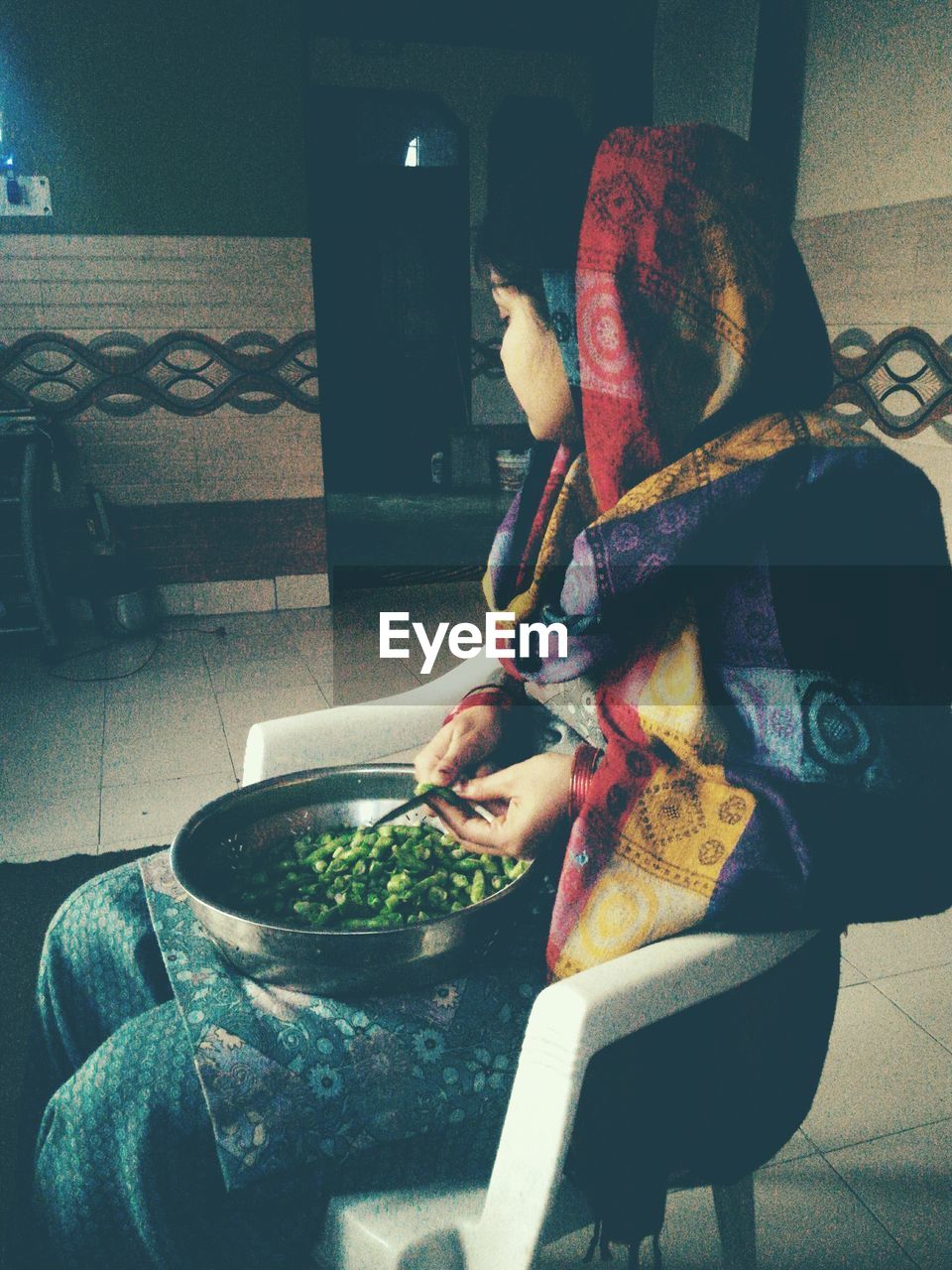 Woman cutting vegetables while sitting on chair at home