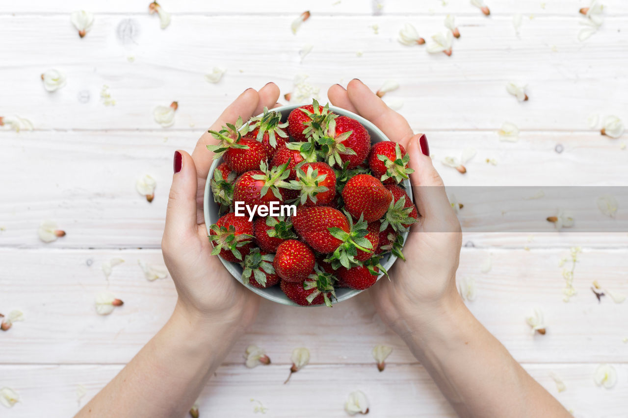 Cropped hands of woman holding strawberries in bowl amidst petals on table