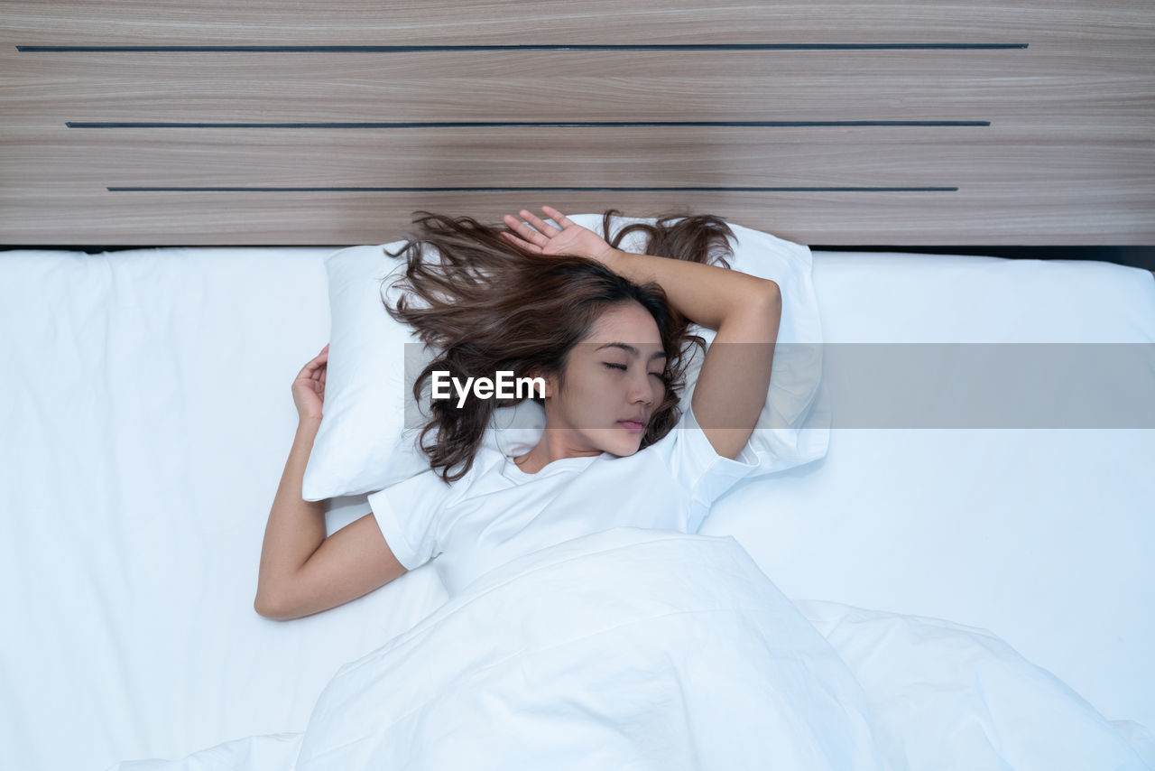 HIGH ANGLE VIEW OF YOUNG WOMAN SLEEPING ON BED