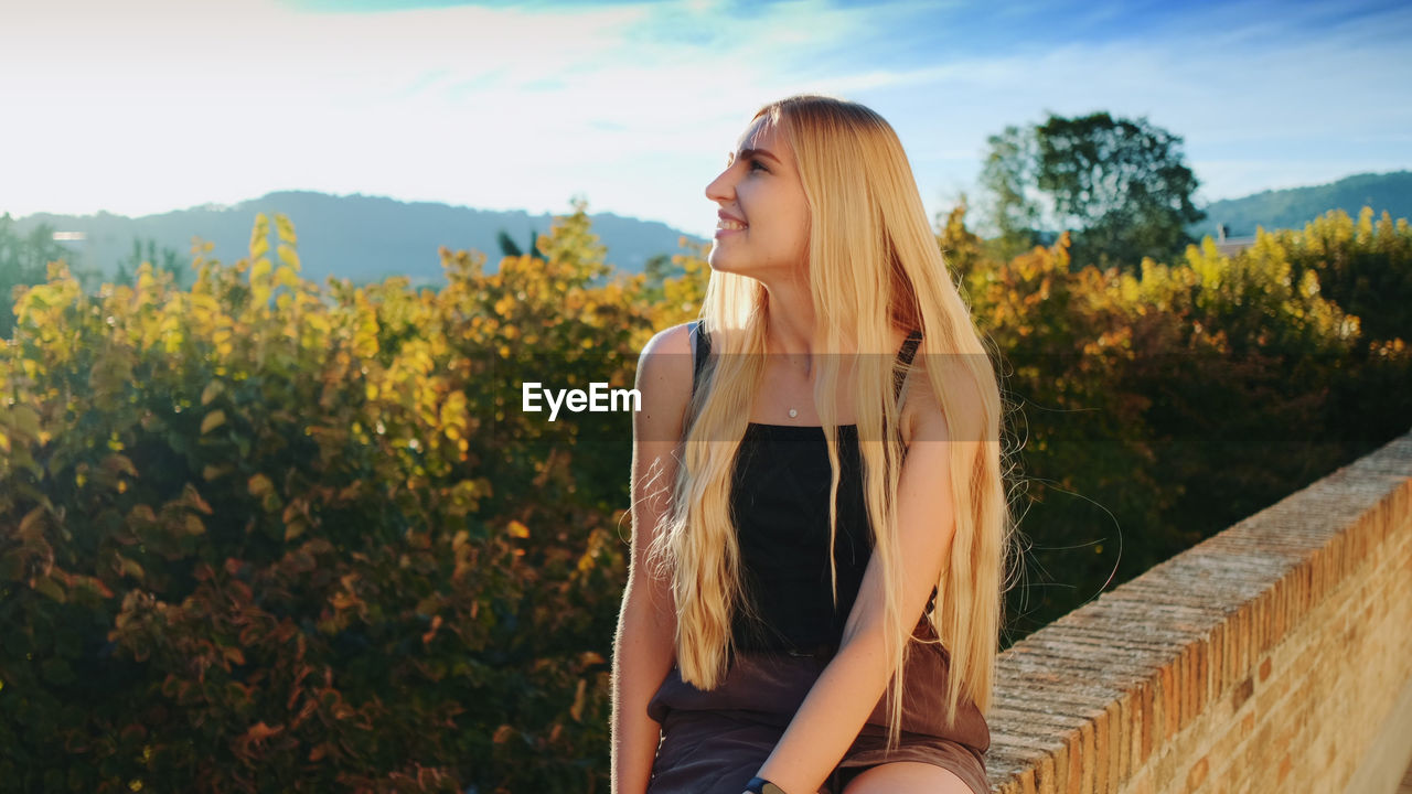 BEAUTIFUL YOUNG WOMAN STANDING BY PLANTS AT PARK