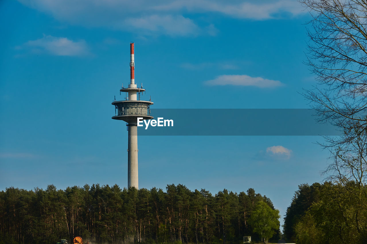 High television tower behind a forest in front of a blue sky