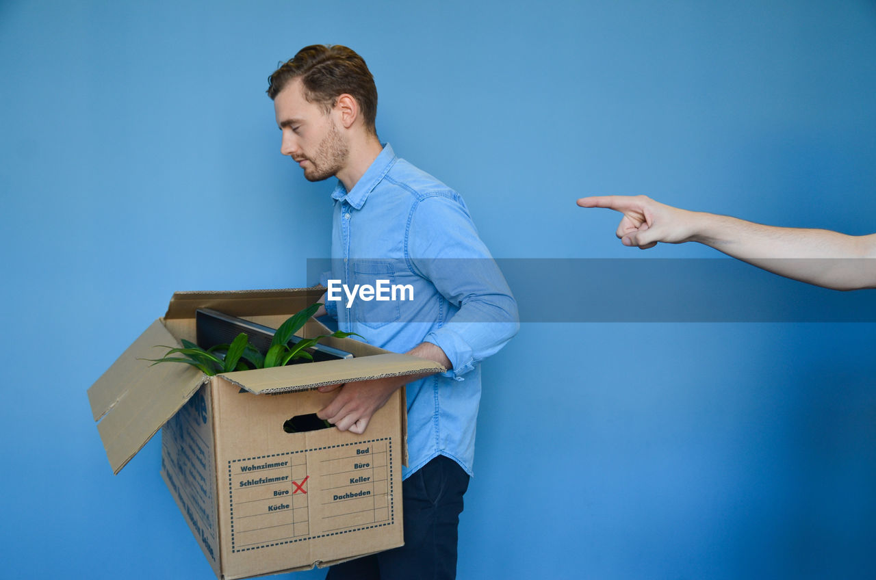 Hand pointing at young man carrying cardboard box after getting fired