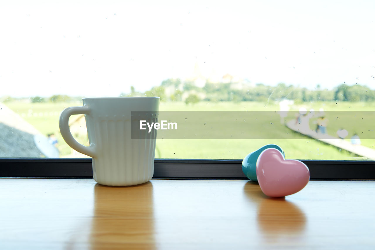 Close-up of coffee cup with heart shapes on window sill