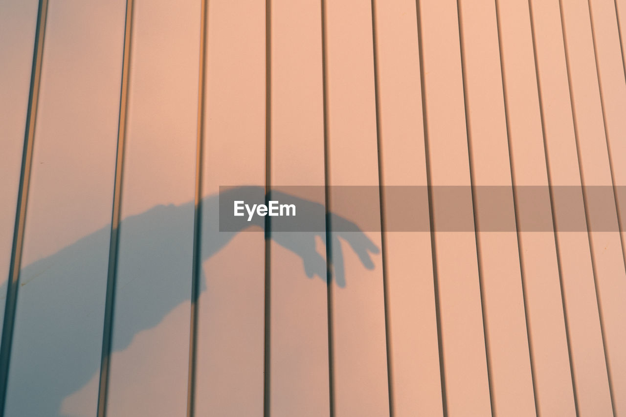 Shadow of a hand illuminated by sunset golden hour against an industrial wall.