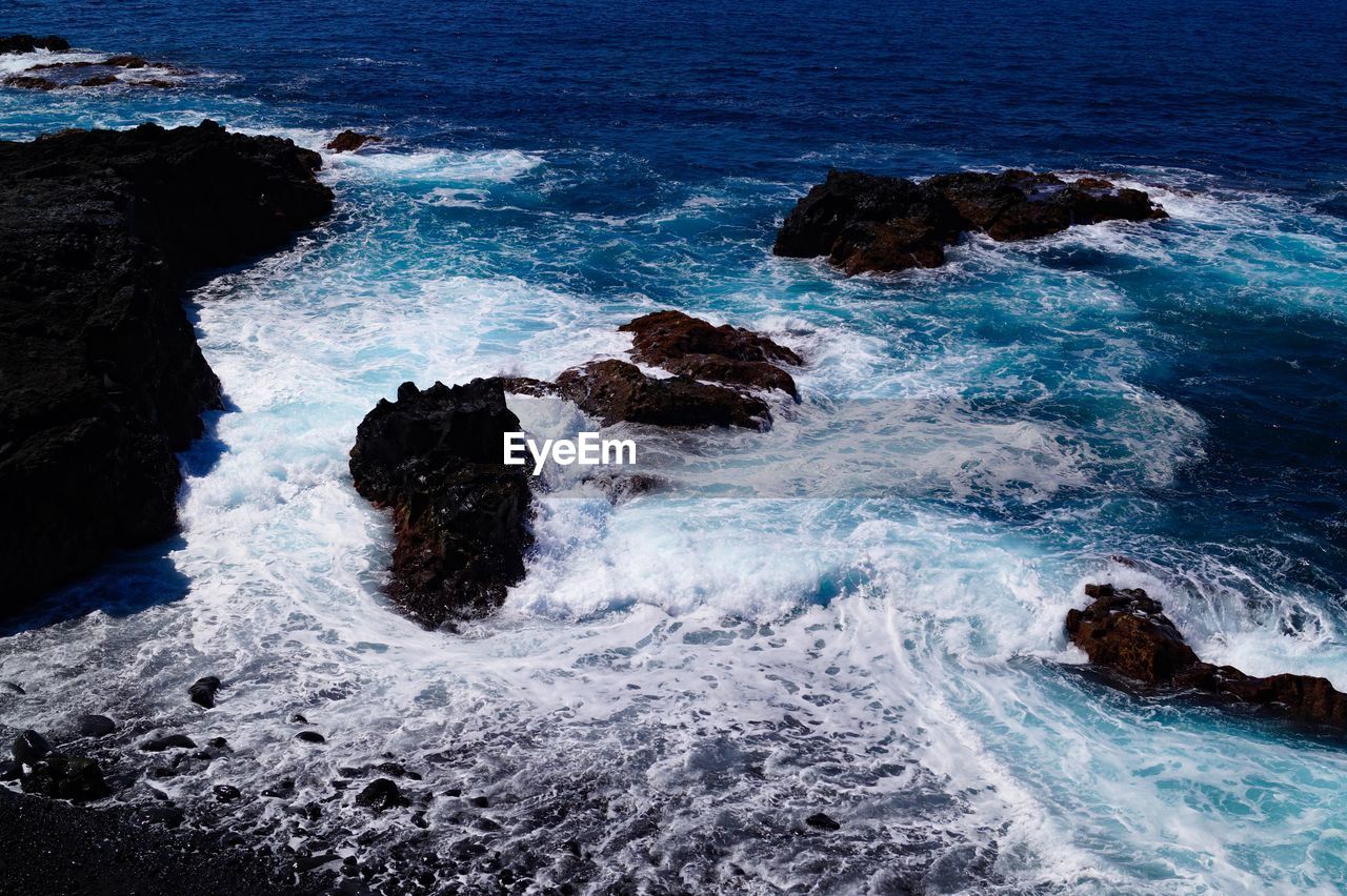 High angle view of waves splashing and crashing  on and over rocks white water surf 