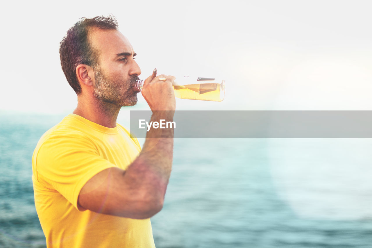 Man drinking beer by sea against sky