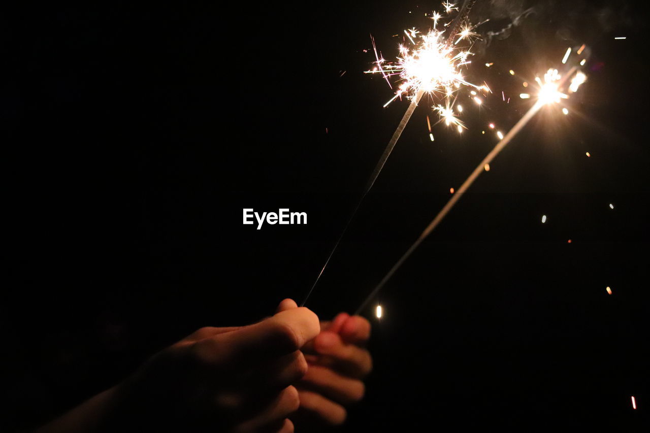 Cropped hands of person holding sparklers at night