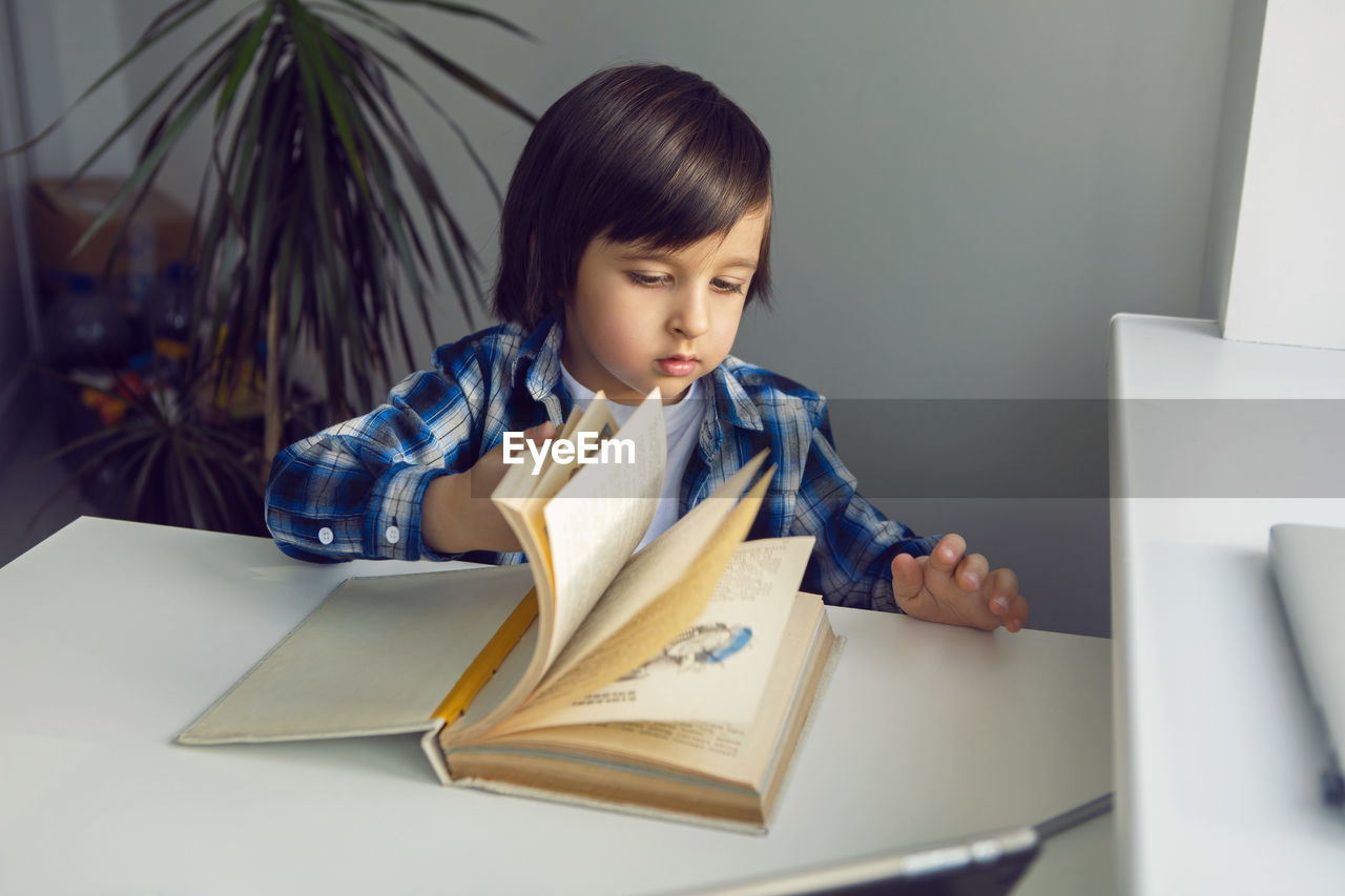 Boy child sits at a desk and learns with a tablet notebook and book