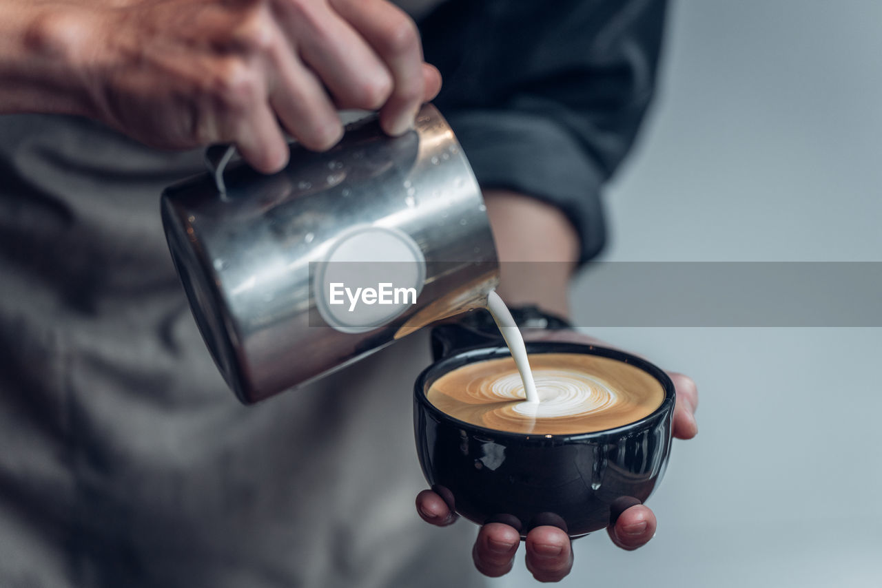 CROPPED IMAGE OF PERSON POURING COFFEE CUP