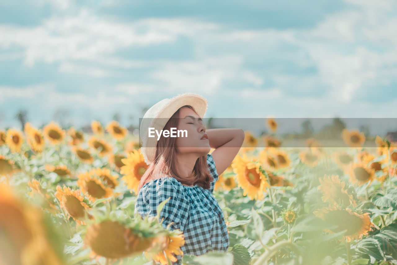 Young woman by sunflowers against sky