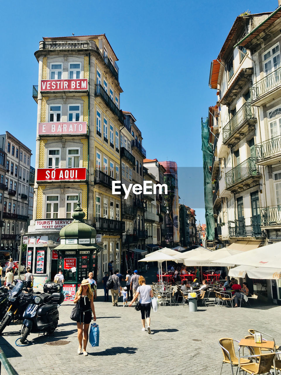 PEOPLE ON CITY STREET AMIDST BUILDINGS AGAINST SKY