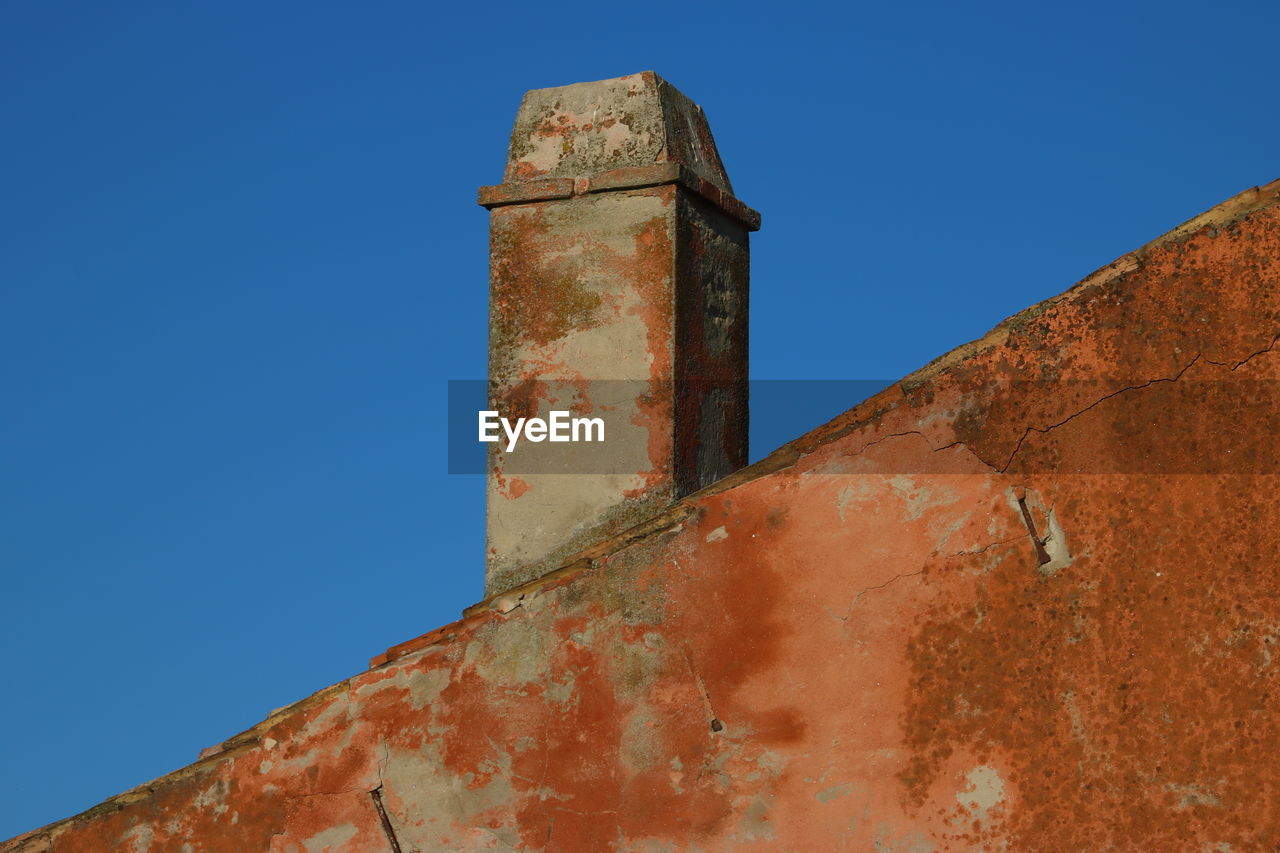 LOW ANGLE VIEW OF OLD RUSTY WALL AGAINST BLUE SKY