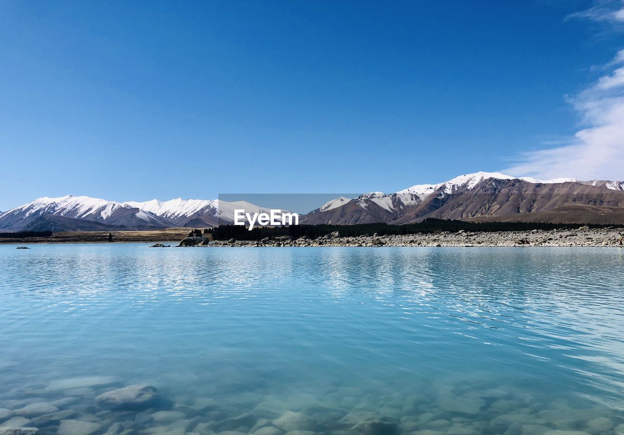 Scenic view of lake and snowcapped mountains against blue sky