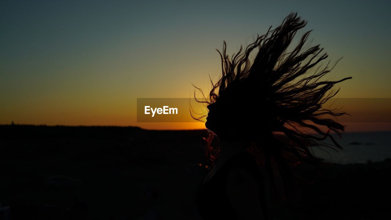 Silhouette woman tossing hair against clear sky during sunset