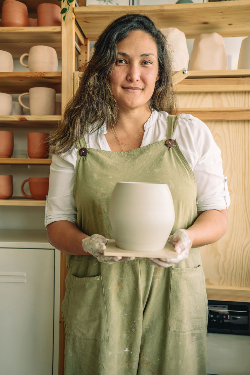 PORTRAIT OF A SMILING YOUNG WOMAN STANDING IN KITCHEN