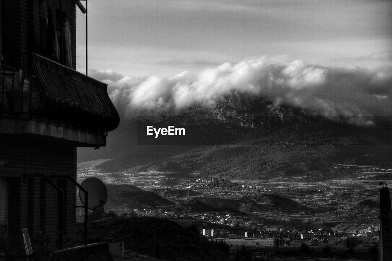 Black and white photo of building wall and mountain landscape with dramatic clouds