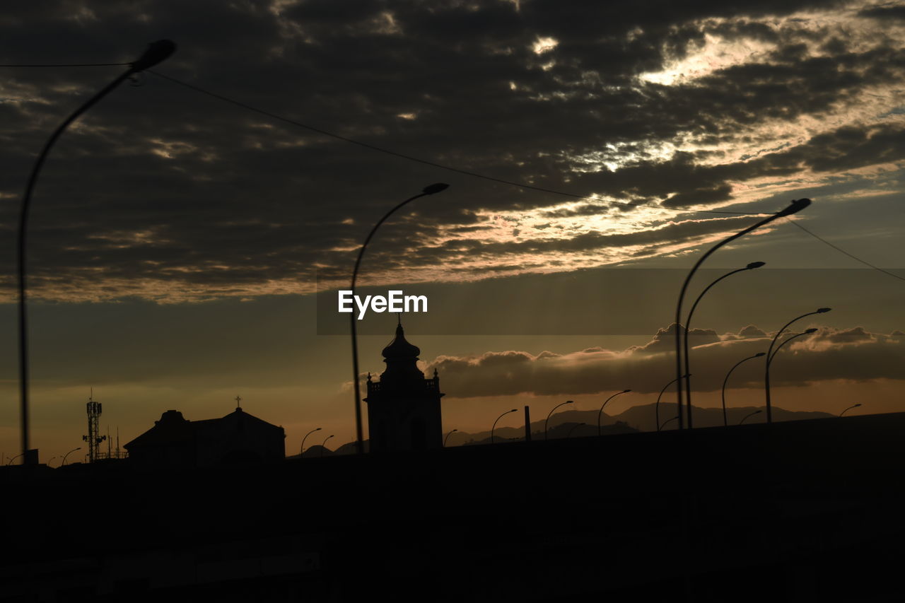 SILHOUETTE OF BUILDINGS AGAINST CLOUDY SKY AT SUNSET