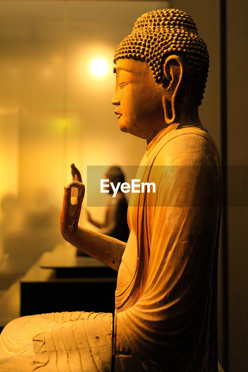 CLOSE-UP OF BUDDHA STATUE AGAINST WALL