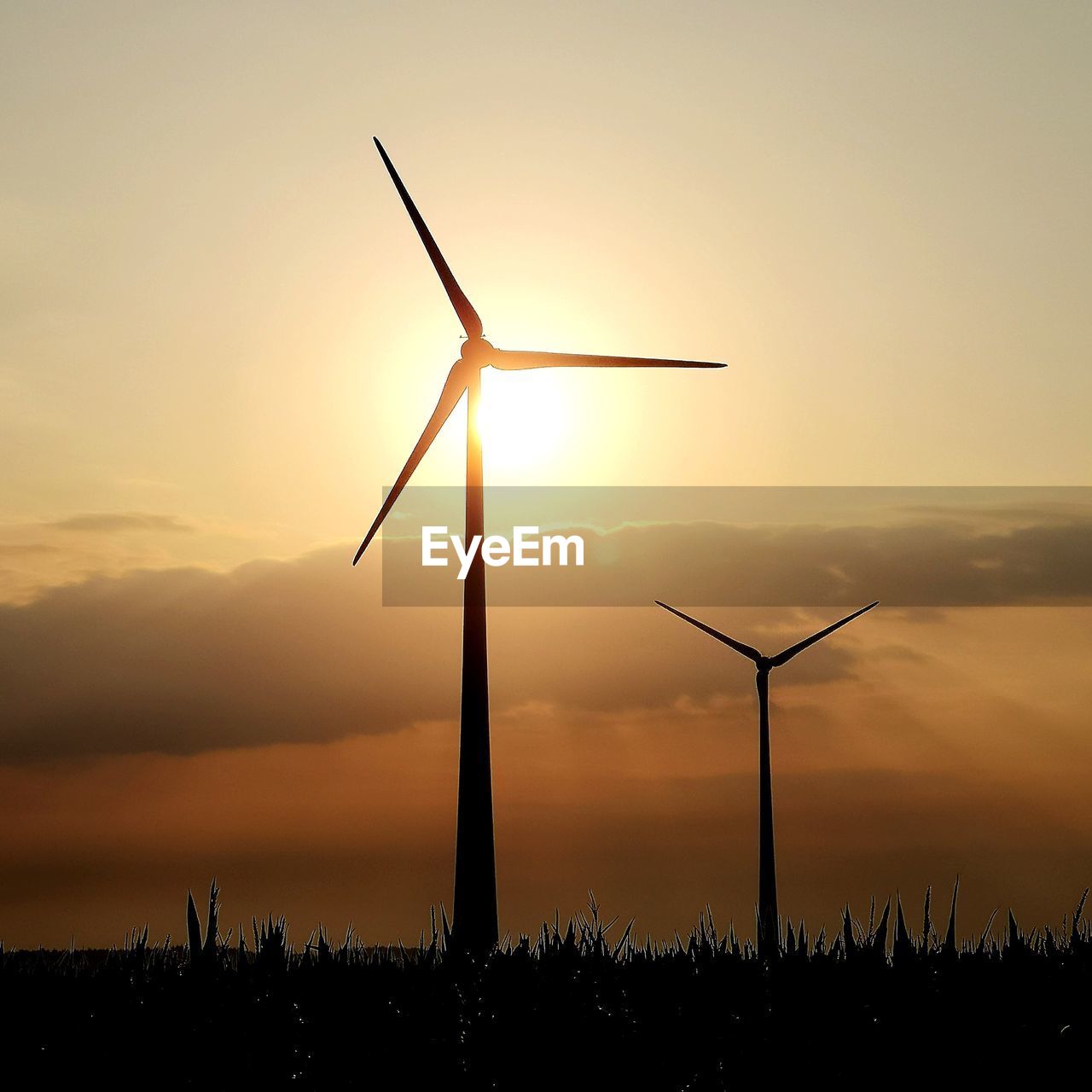 Silhouette windmills on land against sky during sunset