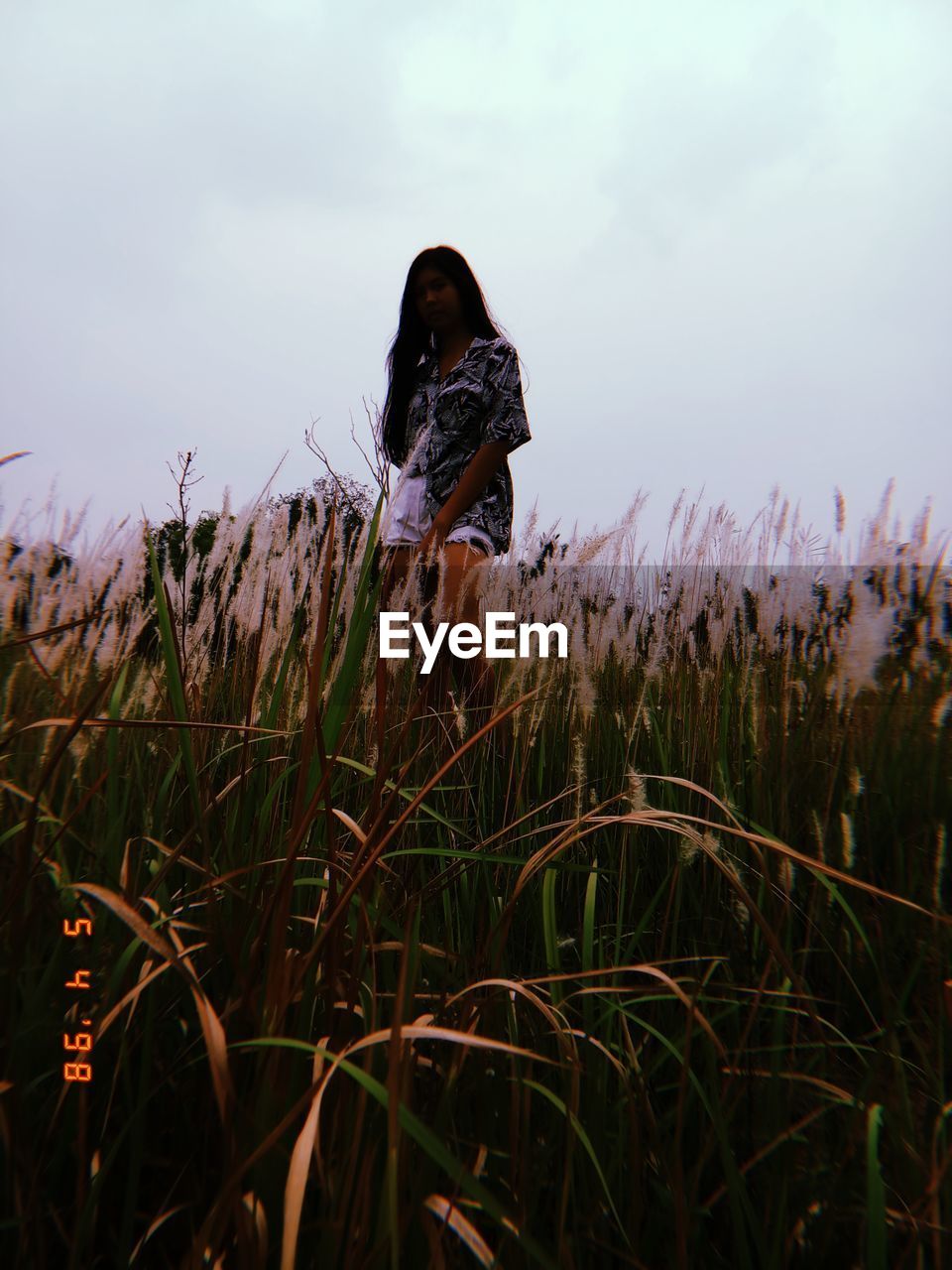 Low angle view of young woman standing on grassy field against sky