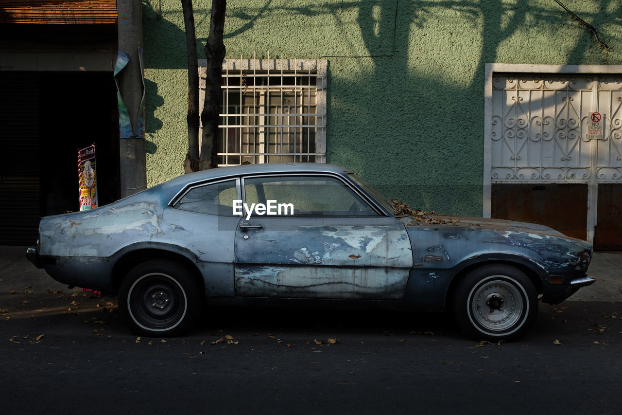 ABANDONED CAR ON STREET BY OLD BUILDINGS IN CITY