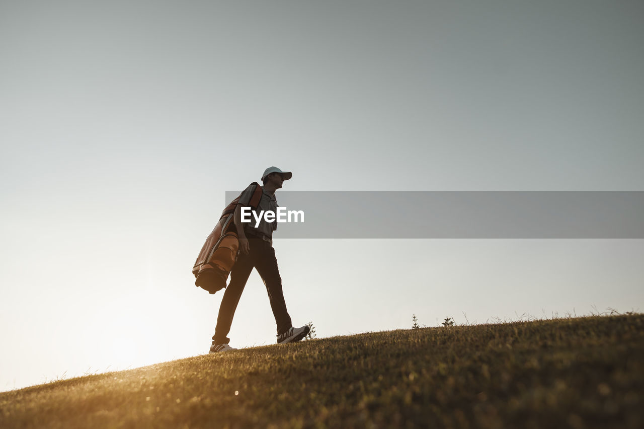 Low angle view of man walking on hill against clear sky