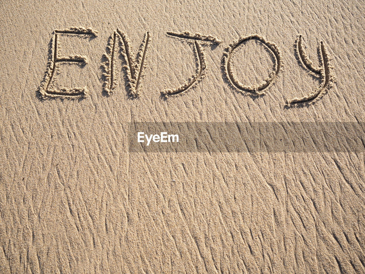 Enjoy word is written on the beach sand with copy space