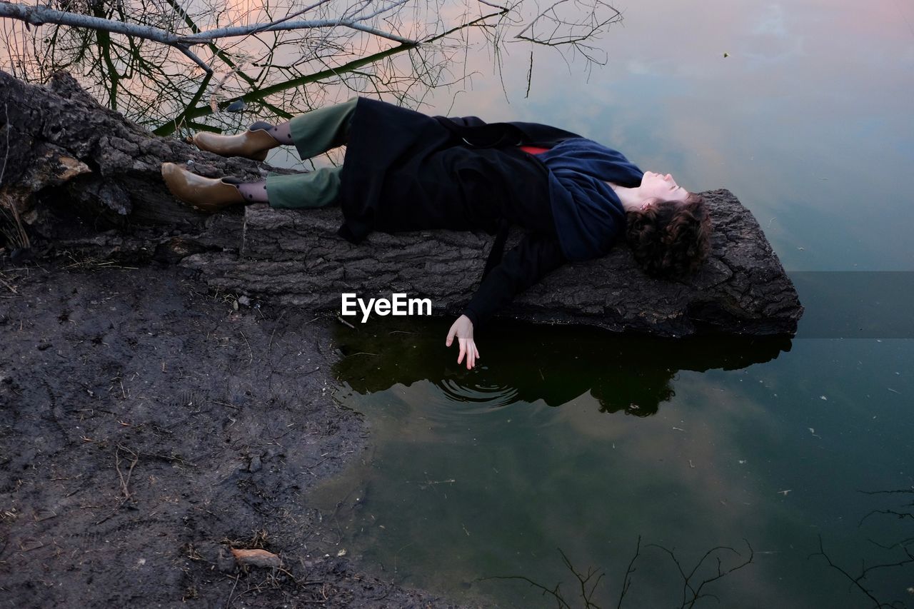 Full length of woman lying on fallen tree trunk by lake